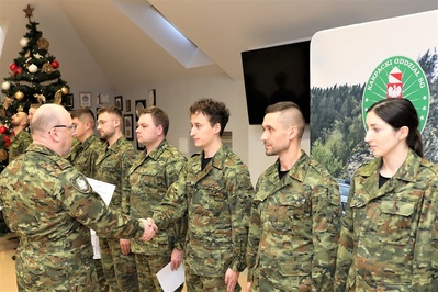 Sala Tradycji KaOSG. W szeregu stoi 8 funkcjonariuszy SG w umundurowaniu polowym. Pułkownik  Marcisz wręcza akt mianowania jednemu z funkcjonariuszy SG.