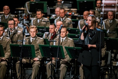 fot. Kinga Ptak, archiwum Małopolskiego Centrum Kultury SOKÓŁ na pierwszym planie pani konferansjer zapowiadająca utwory oraz prowadząca cały koncert noworoczny. na drugim planie muzycy orkiestry reprezentacyjnej straży granicznej.