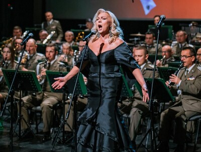 fot. Kinga Ptak, archiwum Małopolskiego Centrum Kultury SOKÓŁ na pierwszym planie zaproszona solistka, występująca w długiej czarnej sukni, wykonująca utwór podczas koncertu. na drugim planie muzycy orkiestry.