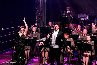 Sala koncertowa. Solista operowy ubrany we frak śpiewa na scenie. Za nim muzycy orkiestry reprezentacyjnej straży granicznej