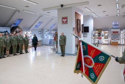 Sala Tradycji karpackiego Oddziału SG. Poczet sztandarowy oraz uczestnicy uroczystości stoją w pozycji na baczność. Odchodzący na emeryturę stoi na baczność.
