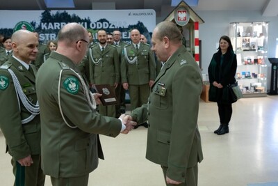 Sala Tradycji karpackiego Oddziału SG. Zastępca komendanta kaosg  pułkownik marek Marcisz  wręcza przyszłemu emerytowi pamiątkową tabliczkę. W tle funkcjonariusze stojący w trzech szeregach, żona funkcjonariusza oraz generał laciuga