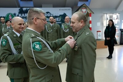 Sala Tradycji karpackiego Oddziału SG. Kapelan kaosg wręcza przyszłemu emerytowi medal milito pro christo  W tle funkcjonariusze stojący w trzech szeregach, żona funkcjonariusza oraz generał laciuga