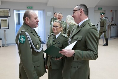 Sala tradycji karpackiego oddziału sg kolezanka i kolega z balic żegnają funkcjonariusza. Wręczają mu pamiątkowy list gratulacyjny.
