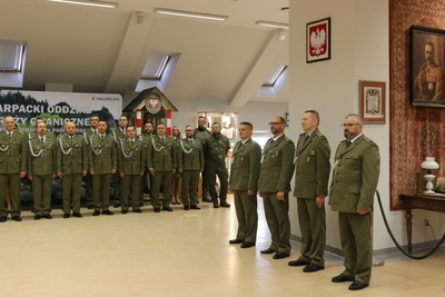 Sala tradycji KaOSG. W szeregu stoi czterech funkcjonariuszy Kaosg odchodzących na emeryturę. W tle kadra kierownicza, koleżankii koledzy funkcjonariuszy stoją w dwuszeregu