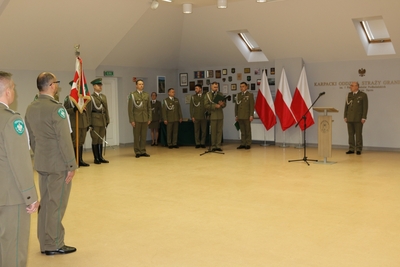 Sala tradycji KaOSG. drugi z odchodzących na emeryturę funkcjonariuszy stoi nw baczność. w tle zastępca komendanta kaosg, poczet sztandarowy i prowadzący uroczystość funkcjonariusze