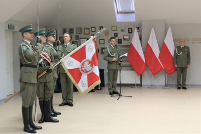 sala tradycji kaosg. zakończenie uroczystości. poczet sztandarowy stoi na baczność, sztandar opuszczony. w tle komendant marcisz i prowadzący uroczystość funkcjonariusze