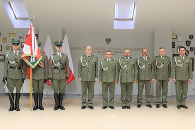 sala tradycji. zdjęcie grupowe, stoją od lewej poczet sztandarowy, komendant marcisz i czterech odchodzących na emeryturę funkcjonariuszy