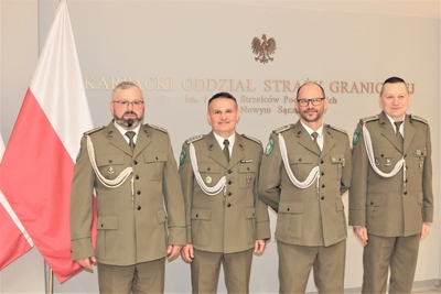 sala tradycji. na tle ściany z napisem karpacki oddział straży granicznej oraz flagi polski stoi czterech funkcjonariuszy sg którzy w dniu dzisiejszym odeszli na emeryturę.