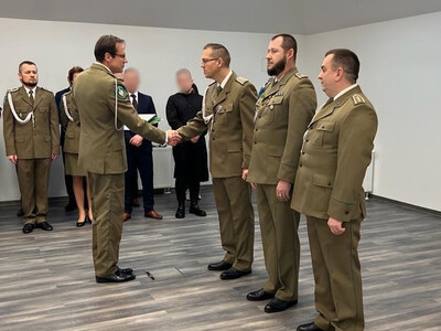sala odpraw placówki sg w tarnowie. komendant wolak wręcza odchodzącemu na emeryturę funkcjonariuszowi pamiątkową tabliczkę. w tle w dwuszeregu pod ścianą stoją funkcjonariusze i pracownicy placówki.