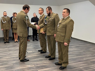 sala odpraw placówki sg w tarnowie. komendant wolak wręcza odchodzącemu na emeryturę funkcjonariuszowi pamiątkową tabliczkę. w tle w dwuszeregu pod ścianą stoją funkcjonariusze i pracownicy placówki.