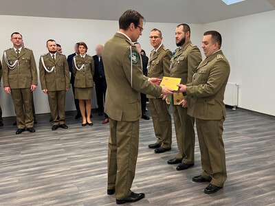 sala odpraw placówki sg w tarnowie. komendant wolak wręcza odchodzącemu na emeryturę funkcjonariuszowi pamiątkową tabliczkę. w tle w dwuszeregu pod ścianą stoją funkcjonariusze i pracownicy placówki.