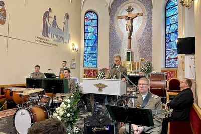 Kościół parafialny Świętego Krzyża i Matki Bożej Nieustającej Pomocy w Tarnowie - Krzyżu. Przy mównicy stoi funkcjonariuszka psg w tarnowie koło niej stoi ksiądz proboszcz, przed nią siedzą muzycy orkiestry reprezentacyjnej straży granicznej, w tle ołtarz