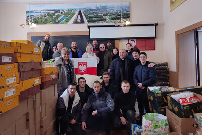 Wolontariusze i obdarowani stoją w grupie w jednym z pomieszczeń Domu polskiego w Zaporożu , kilkoro trzyma polską flagę. Obok nich bardzo dużo pudeł z zakupioną żywnościa i pomocą humanitarną.