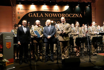 na scenie stoją muzycy orkiestry, starosta sądecki, przewodniczący rady powiatu, komendant karpackiego oddziału straży granicznej oraz naczelnik orkiestry reprezentacyjnej straży granicznej, który trzyma w rekach statuetkę złotego jabłka sądeckiego.