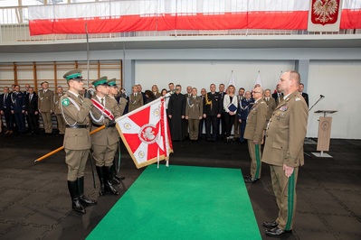 Komendant odchodzący na emeryturę i komendant obejmujący stanowisko Komendanta Karpackiego Oddziału Straży Granicznej stojący przed Sztandarem Karpackiego Oddziału Straży Granicznej. Na drugim planie stoją zaproszeni goście i przyglądają się przekazaniu sztandaru nowemu Komendantowi.