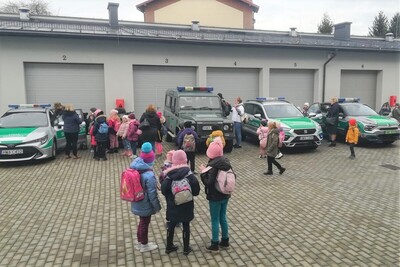 Na placu przed placówka sg w tarnowie dzieci przyglądają się samochodom sg prezentowanym przez funkcjonariuszy. cześć dzieci wsiada do pojazdów, część ogląda je z zewnątrz. w lte garaże placówki sg w tarnowie.