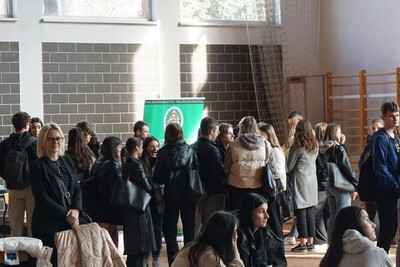 sala gimnastyczna 1 lo w suchej beskidzkiej. przed stoiskiem promocyjnym kaosg stoi  grupa około 40 tegorocznych maturzystów - uczestników targów zawodów mundurowych