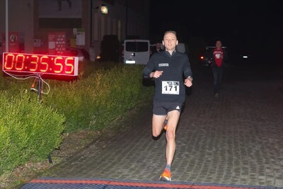 Funkcjonariusz Kaosg w stroju sportowym wbiega po zmroku przez metę. Wyświetla się czas 00:00:35:55 Za nim biegnie mężczyzna