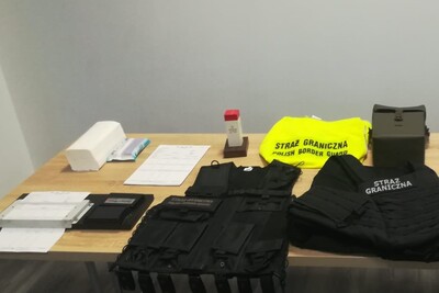 na stole leży sprzęt służbowy na co dzień wykorzystywany przez funkcjonariuszy sg. Są m.in. kamizelka odblaskowa, kamizelka taktyczna, zestaw do daktyloskopii oraz słupek graniczny