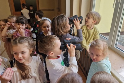 dzieci wyglądające przez okno używając służbowej lornetki, obok inne zebrane dzieci.
