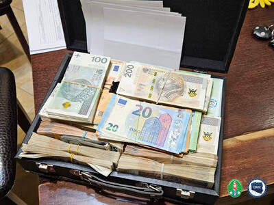 Na stole leży walizka z dużą ilością pieniędzy. Pliki banknotów spiętych gumkami o nominale 100 zł, 200 zł i 20 euro. W prawym dolnym rogu, logotyp Karpackiego Oddziału Straży Granicznej i Centralnego Biura Zwalczania Cyberprzestępczości.