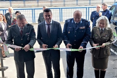 Uczestnicy uroczystości stoją przed budynkiem. Przedstawiciele strony słowackiej i polskiej trzymają w rękach nożyczki, przygotowując się do przecięcia uroczyście szarfy.