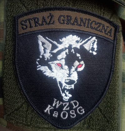 Szkolenie "kondycyjno-taktyczne" funkcjonariuszy KaOSG emblemat wydziału zabezpieczenia działań karpackiego oddziału straży granicznej, przedstawia on głowę wilka po środku. pod głową skrót wydziału czyli WZD KaOSG a nad głowo napis Straż graniczna. tło emblematu jest czarne.