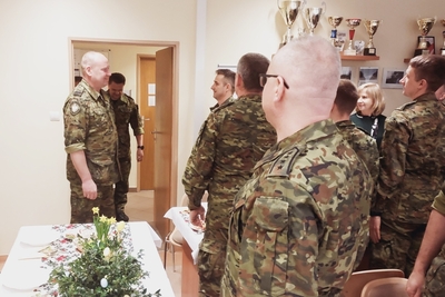 na pierwszym planie stoi komendant Karpackiego Oddziału straży granicznej, który przyjmuje meldunek od funkcjonariusza straży granicznej. Całej sytuacji przyglądają się zebrani podczas spotkania świątecznego funkcjonariusze oraz pracownicy zakopiańskiej placówki straży granicznej. Przed nimi stoi stół na którym znajduję się biały obrus oraz ozdoba świąteczna.