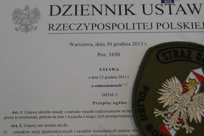 Na wydrukowanej ustawie o cudzoziemcach leży plakietka funkcjonariusza straży granicznej