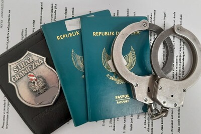 Dwóch obywateli Indonezji nielegalnie w Polsce kajdanki położone na dwóch paszportach Indonezji  w kolorze zielonym ze złotymi napisami i złotym godłem  Indonezji obok paszportów znajduje się odznaka funkcjonariusza straży granicznej. wszystko umieszczone jest na pouczeniu wydanym przez funkcjonariuszy straży granicznej.