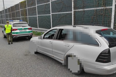 Rekordzista wśród nielegalnie przebywających cudzoziemców na terytorium RP zatrzymany pojazd na autostradzie przez funkcjonariuszy straży granicznej. pojazd znajduje się na pierwszym planie jest w kolorze srebrnym przed nim stoi służbowy pojazd straży granicznej obok którego stoi funkcjonariuszka straży granicznej.