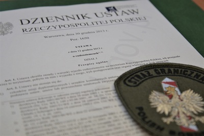 Filipińczycy przeholowali swój pobyt w Polsce emblemat straży granicznej z napisem straż graniczna w górnej jego części oraz słupkiem granicznym w kolorach czerwono białym oraz orłem białym poniżej napis polish. emblemat znajduje się na papierowej wersji ustawy o cudzoziemcach.