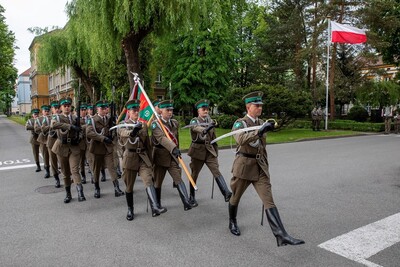 kompania honorowa straży granicznej idzie przemarszem podczas uroczystości. w tle powiewa biało czerwona flaga Polski.
