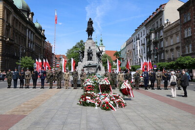 Grób Nieznanego Żołnierza na Placu Matejki w Krakowie w biało-czerwonych barwach. Przed pomnikiem stoi warta honorowa wystawiona przez każdą ze służb mundurowych małopolski