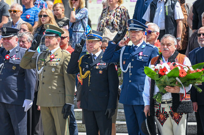 uczestnicy uroczystości stoją na baczność śpiewają hymn polski. przedstawiciele służb mundurowych oddają honor