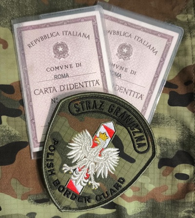 Syryjczycy z podrobionymi włoskimi dokumentami emblemat straży granicznej, na którym widnieje napis Straż Graniczna, pod nim znajduje się orzeł biały na słupku granicznym, który jest w kolorach białym i czerwonym pod nim jest napis Polish Border Quard. emblemat położony jest na włoskich dowodach osobistych. całość położona jest na materiale w kolorze moro.