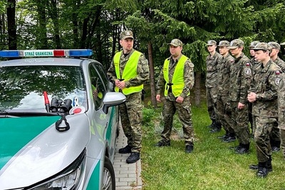 Funkcjonariusze SG stoją przy samochodzie. Prowadzą pogadankę dla młodzieży w mundurach