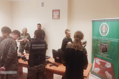 W auli placówki sg w zakopanem uczniowie przeglądają sprzęt służbowy położony na stołach. nadzoruje ich funkcjonariusz sg