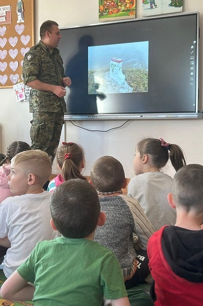 przedszkole. funkcjonariusz stoi przed ekranem, na którym wyświetla się zdjęcie znaku granicznego. dzieci słuchają z zaciekawieniem.