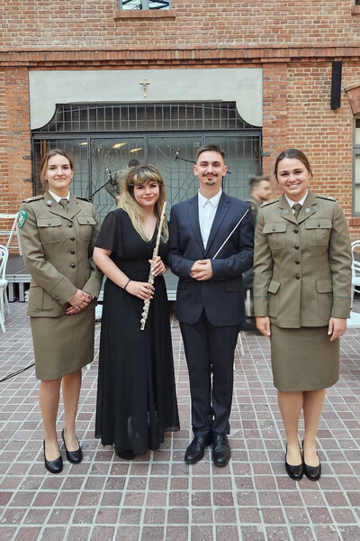 funkcjonariusz straży granicznej pozujący do wspólnego zdjęcia po wykonanym egzaminie z dyrygentury. towarzysza mu trzy kobiety w tym jedna flecistka oraz dwie funkcjonariuszki z Placówki Straży Granicznej w Krakowie.