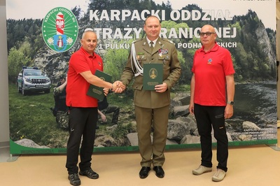 Sala Tradycji KaOSG. Na tle baneru z napisem KaOSG stoi dwóch przedstawicieli GOPR  i Komendant KaOSG. Składają sobie gratulacje w związku z podpisanym porozumieniem.