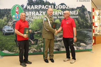 Sala Tradycji KaOSG. Na tle baneru z napisem KaOSG stoi dwóch przedstawicieli GOPR  i Komendant KaOSG. Składają sobie gratulacje w związku z podpisanym porozumieniem