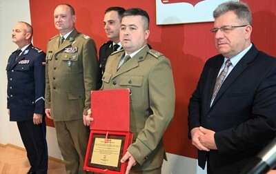 Uczestnicy spotkania stoją w szeregu. Wyróżniony funkcjonariusz trzyma w ręku pamiątkowy grawerton.