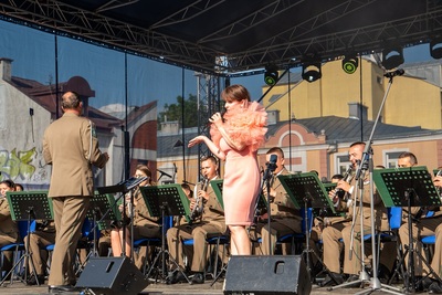 solistka orkiestry reprezentacyjnej straży granicznej wykonuje utwór.  w tle znajdują się muzycy orkiestry którzy koncert wykonują na siedząco. orkiestra dyryguje jej naczelnik.