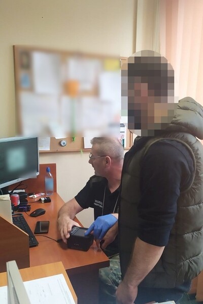 Na zdjęciu znajduje się zatrzymana osoba od której, funkcjonariusz straży granicznej pobiera odciski linii papilarnych.