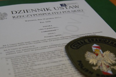 Na pierwszej stronie ustawy o cudzoziemcach leży plakietka z orzełkiem oraz napisem straż graniczna.
