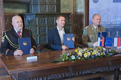 Podpisujący porozumienie trzej partnerzy projektu trzymają teczki z dokumentami oparte na stole i uśmiechają się