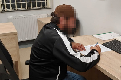 jeden z zatrzymanych mężczyzn siedzi przy biurku i podpisuje protokół zatrzymania.