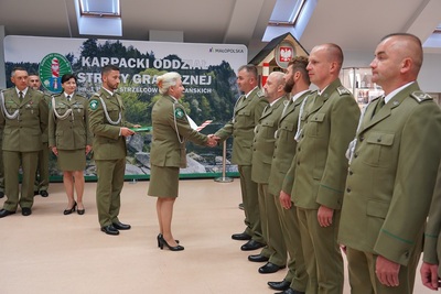 Pani Komendant karpackiego Oddziału straży granicznej wręcza akty mianowań na pierwszy stopień w korpusie chorążych funkcjonariuszom straży granicznej. w tle widoczny baner promocyjny oddziału.